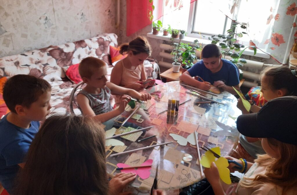 Учасники майстер-класу сидять за круглим столом і виготовляють з різнокольорового паперу своїх метеликів
